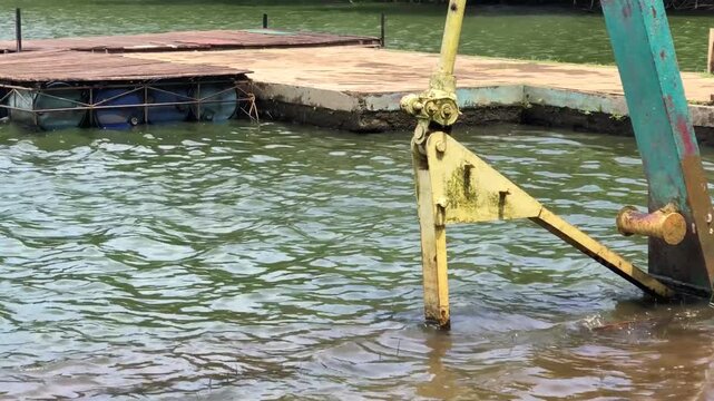 Old metal mechanism beside floating dock structure on water, showing industrial engineering details, marine equipment, and aging infrastructure for construction, maintenance, and environmental