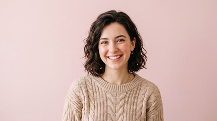 Fototapeta premium Portrait of a smiling young woman wearing a chunky knit sweater against a pink background with well being, portrait