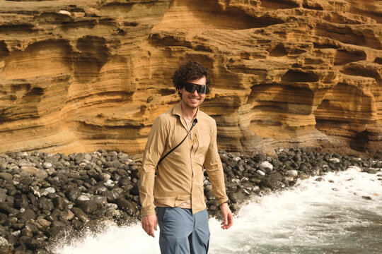 Man walking along a rocky beach with volcanic cliffs in the background