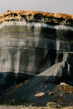 A dark volcanic cliff in Lanzarote with golden-brown sediment layers.