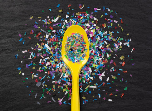 Microplastic in on a plastic spoon on black slate background,  close up, top view