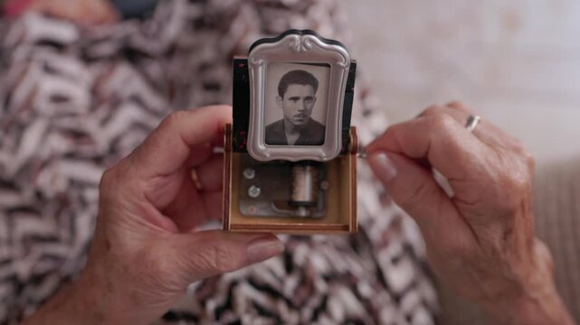point of view of a Nostalgic senior woman's hands turning the crank on a vintage music box, which holds a black and white portrait of a man, evoking sweet memories and timeless romance from the past