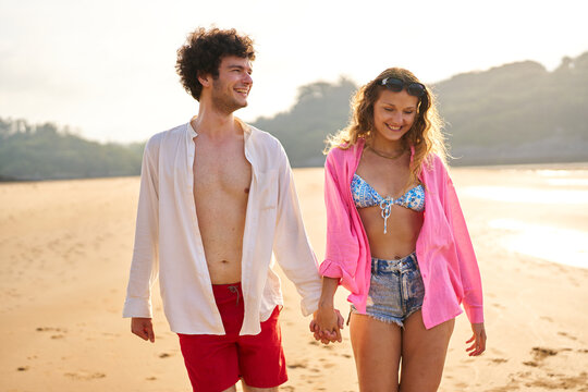 Smiling couple holding hands walking on beach at sunset