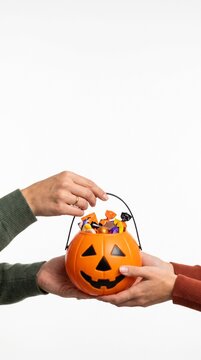 Hands exchanging a full pumpkin candy bucket on white background for Halloween trick or treating