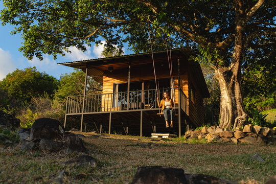 Woman relaxing on swing by wooden cabin in nature