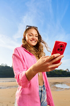 Young woman smiling using smartphone at beach