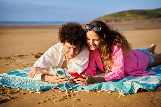 Happy couple relaxing on beach scrolling smartphones