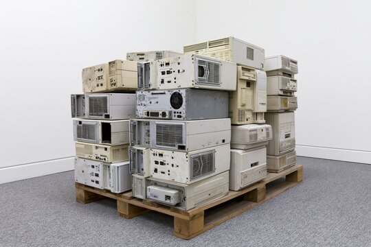 The stack of vintage computer hardware on a wooden pallet in a white room
