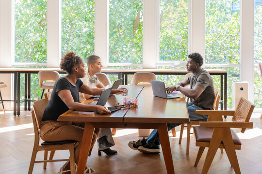 Three People Sit Around a Wooden Table in a Modern Office