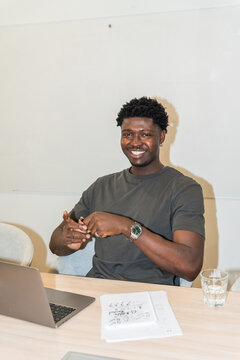 Black Man Sitting at a Table Smiling While Working on a Laptop