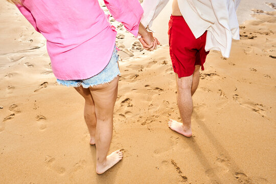 Couple holding hands walking along beach leaving footprints