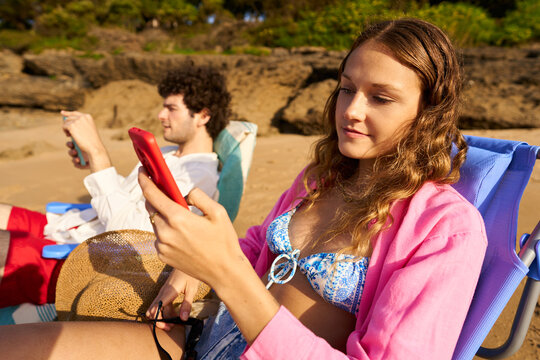 Couple relaxing on beach chairs using smartphones