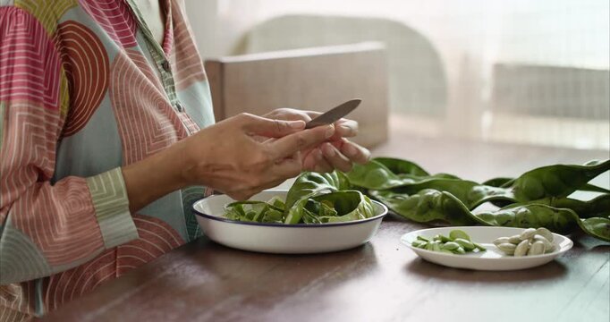 Close up. Asian Woman Hand Peeling Parkia Speciosa , Stink Bean, Bitter Bean, with Knife into White Plate on Table.