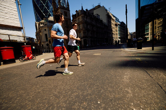 Men jog side by side on a bright street in the city of London