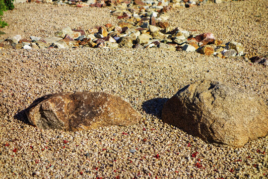 A row of large, weathered granite boulders set on a bed of fine gravel in a desert-style xeric ground, natural background, backdrop