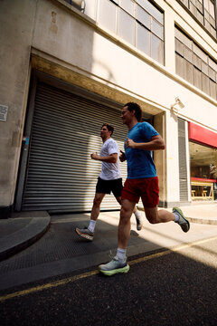 Men jog side by side on a bright street.