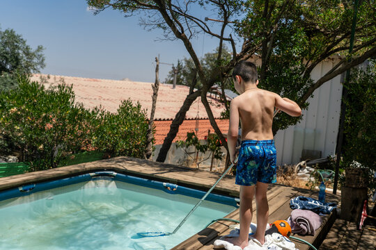 Kid Skimming A Backyard Pool With A Leaf Net On A Hot Summer Day