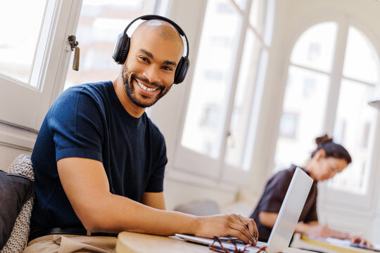 Smiling man in headphones working on laptop at bright coworking