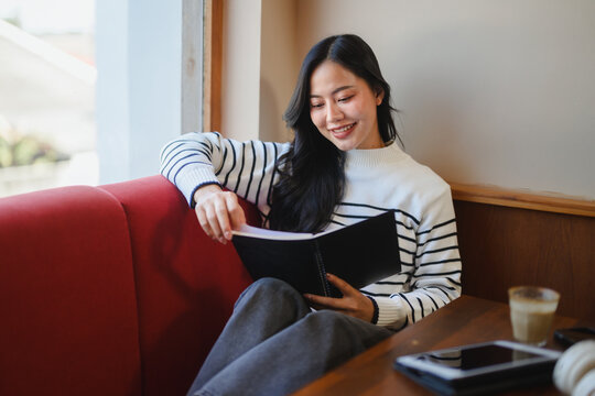 Smiling woman reading notebook in cafe by window