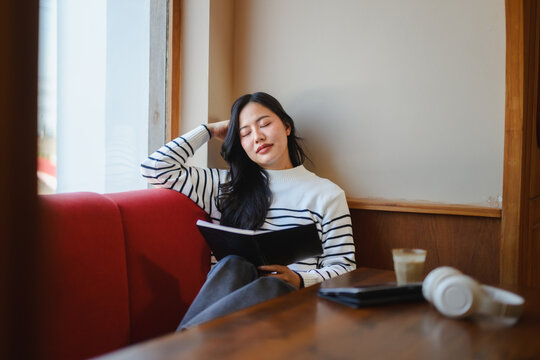 Young woman relaxing by window reading book in cafe