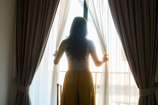 Woman opening curtains looking out at new day