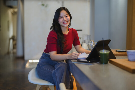 Young Asian woman smiling, working with tablet in cafe