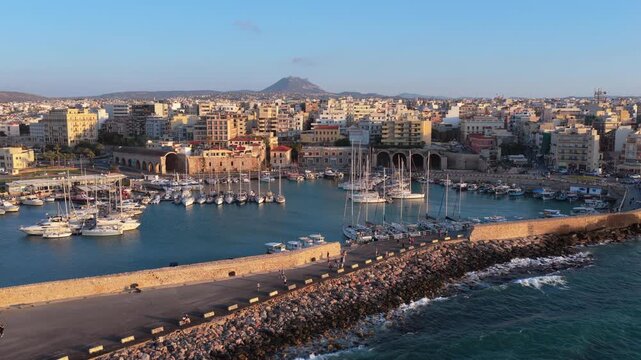 Aerial drone view of the Venetian harbor and its arched arsenals below the city at golden hour, Heraklion, Greece