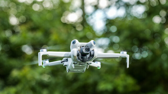 Modern drone with camera in flight against a blurred green background of trees