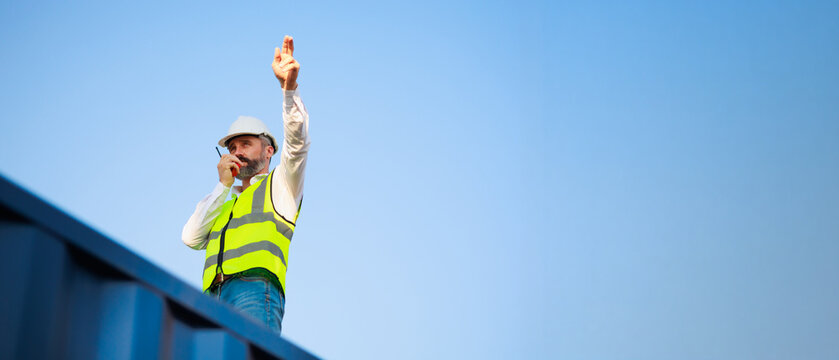 Handsome caucasian male dock foreman worker in white hard hat helmet and high-visibility vest working in Shipping Cargo Container Terminal Depot