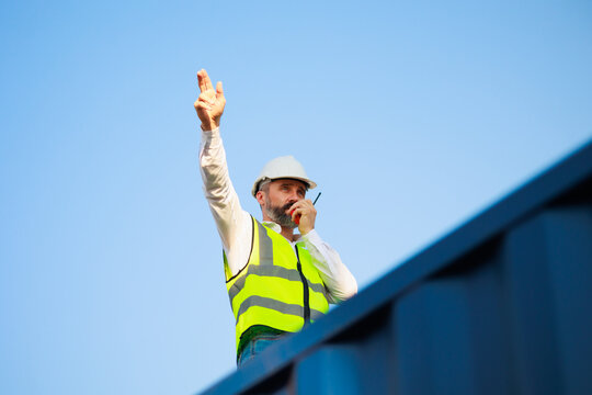 Handsome caucasian male dock foreman worker in white hard hat helmet and high-visibility vest working in Shipping Cargo Container Terminal Depot