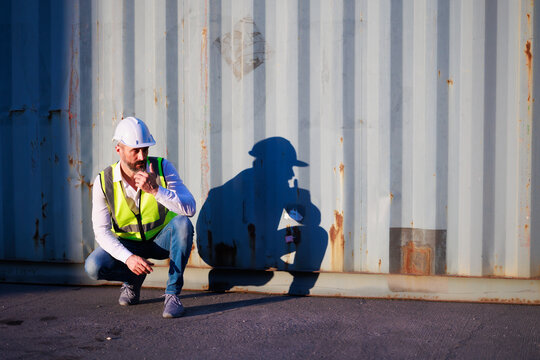 Handsome caucasian male dock foreman worker in white hard hat helmet and high-visibility vest working in Shipping Cargo Container Terminal Depot