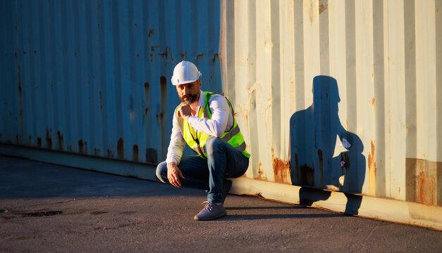 Handsome caucasian male dock foreman worker in white hard hat helmet and high-visibility vest working in Shipping Cargo Container Terminal Depot
