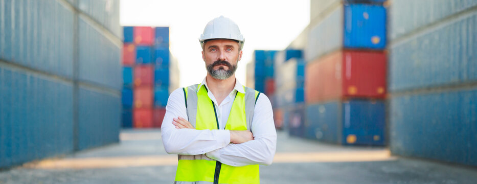Man manager cross arm. Handsome caucasian male dock foreman worker in white hard hat helmet and high-visibility vest walking in Shipping Cargo Container Terminal Depot