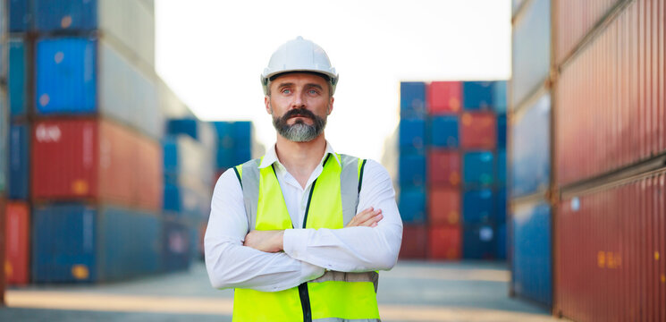 Man manager cross arm. Handsome caucasian male dock foreman worker in white hard hat helmet and high-visibility vest walking in Shipping Cargo Container Terminal Depot