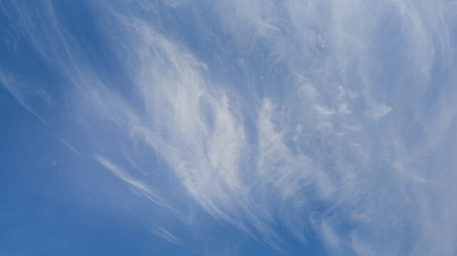 Wispy cirrus clouds drift across a clear blue sky on a bright day