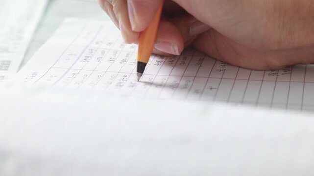 사무실에서 업무 장부에 꼼꼼하게 수치를 확인하며 정산 내역을 필기하는 모습입니다.