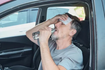 Man feeling sick from heat, drinking water and cooling forehead with cold compress in car © colnihko