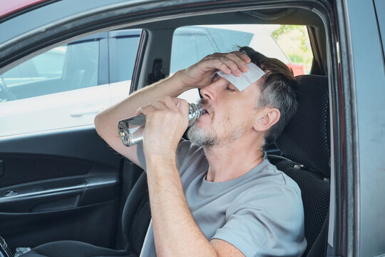 Man feeling sick from heat, drinking water and cooling forehead with cold compress in car