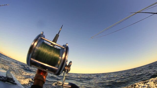 Sunset fishing reel on deep sea boat trolling for big game fish in 4K Ultra HD footage

