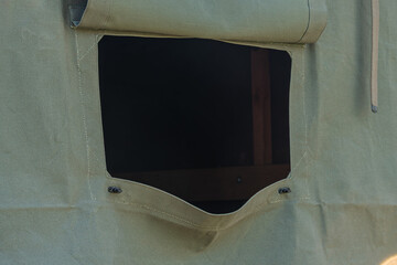 Close-up view of canvas shelter featuring olive green fabric, durable stitching, dark wooden frame, rectangular opening, metal grommets, textured material, outdoor setting, camping adventure, privacy © Mister