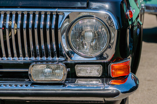 Vintage vehicle front view, emphasizing polished chrome grille, round headlight assembly, fog lights, smooth bumper, deep glossy green paint finish, outdoor setting, blurred background, classic