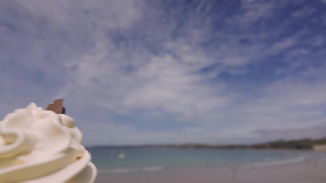 POV of a hand holding a delicious melting Ice cream cone over the beach in Newquay, Cornwall, England on a sunny June day, a sea gull swoops on the ice cream at end end.