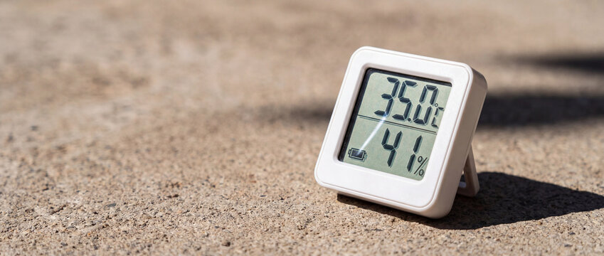 White digital thermometer on hot concrete displaying high summer temperature and low humidity, perfect for weather monitoring, climate change articles, and heatwave safety guides
