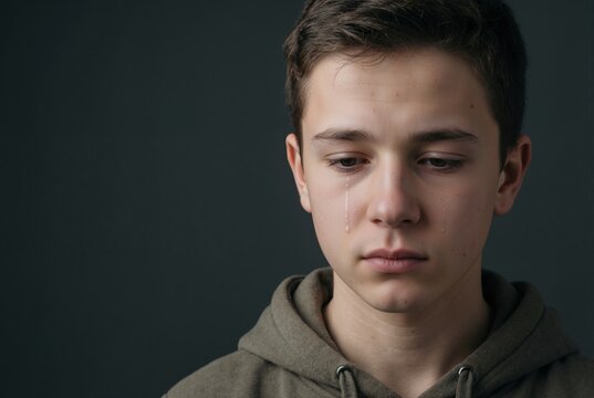 Vertical portrait of sad teenage boy crying. Young male in brown hoodie with tears on his face. Depression and emotional distress concept