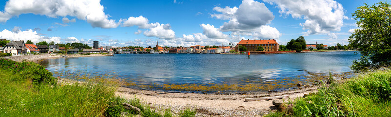 Panoramic view of Sonderborg harbor with historic old town, beach, shoreline vegetation and dramatic summer clouds along Flensburg Fjord. © EKH-Pictures