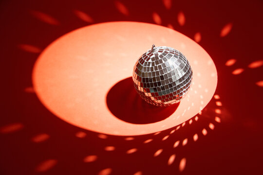 Shiny disco ball, also known as mirror ball, on a red surface with scattered light reflections. Disco ball decoration with light reflections on vibrant red background