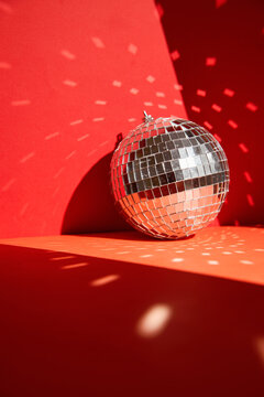 Shiny disco ball, also known as mirror ball, on a red surface with scattered light reflections. Disco ball decoration with light reflections on vibrant red background
