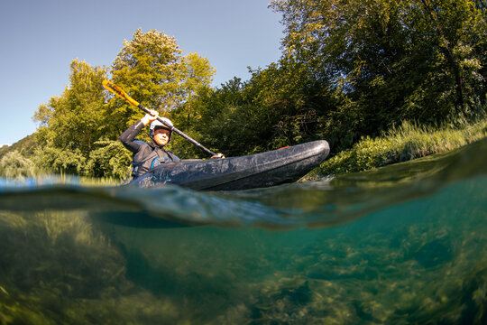 Whitewater kayaking in a river surrounded by trees during a clear day with sunlight