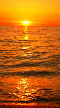 Sunset ocean beach scene featuring golden waves washing onto the pebble shore under a brilliant orange evening sky for a peaceful mood