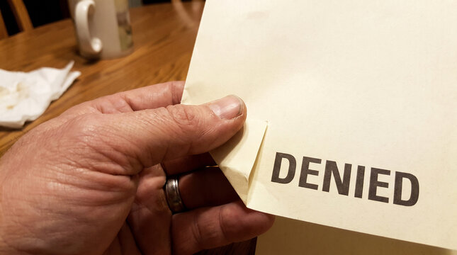 Hand holding document with denied stamp text on paper
